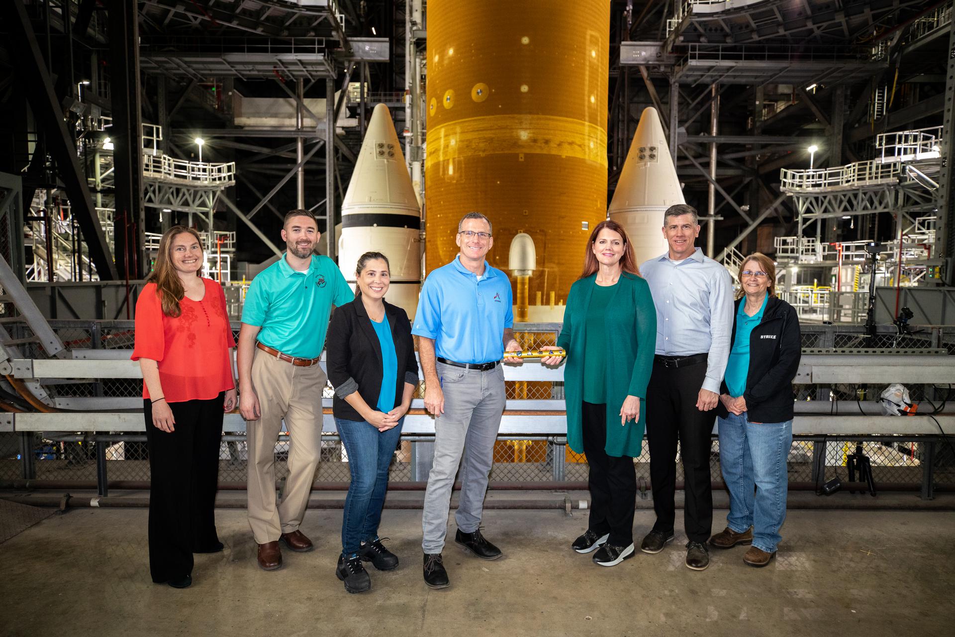 Cliff Lanham, keempat dari kiri, manajer operasi darat di Exploration Ground Systems (EGS), menyerahkan tongkat estafet kepada Charlie Blackwell-Thompson, direktur peluncuran Artemis I, di dalam Gedung Perakitan Kendaraan di Kennedy Space Center NASA di Florida pada 16 Maret 2022. Bergabung dengan mereka dari kiri, adalah Stacey Bagg, Matt Czech, dan Liliana Villareal, dengan EGS. Di sebelah Blackwell-Thomson adalah Jeremy Graeber, wakil direktur peluncuran, dan Teresa Annulis. (NASA/Glenn Benson)