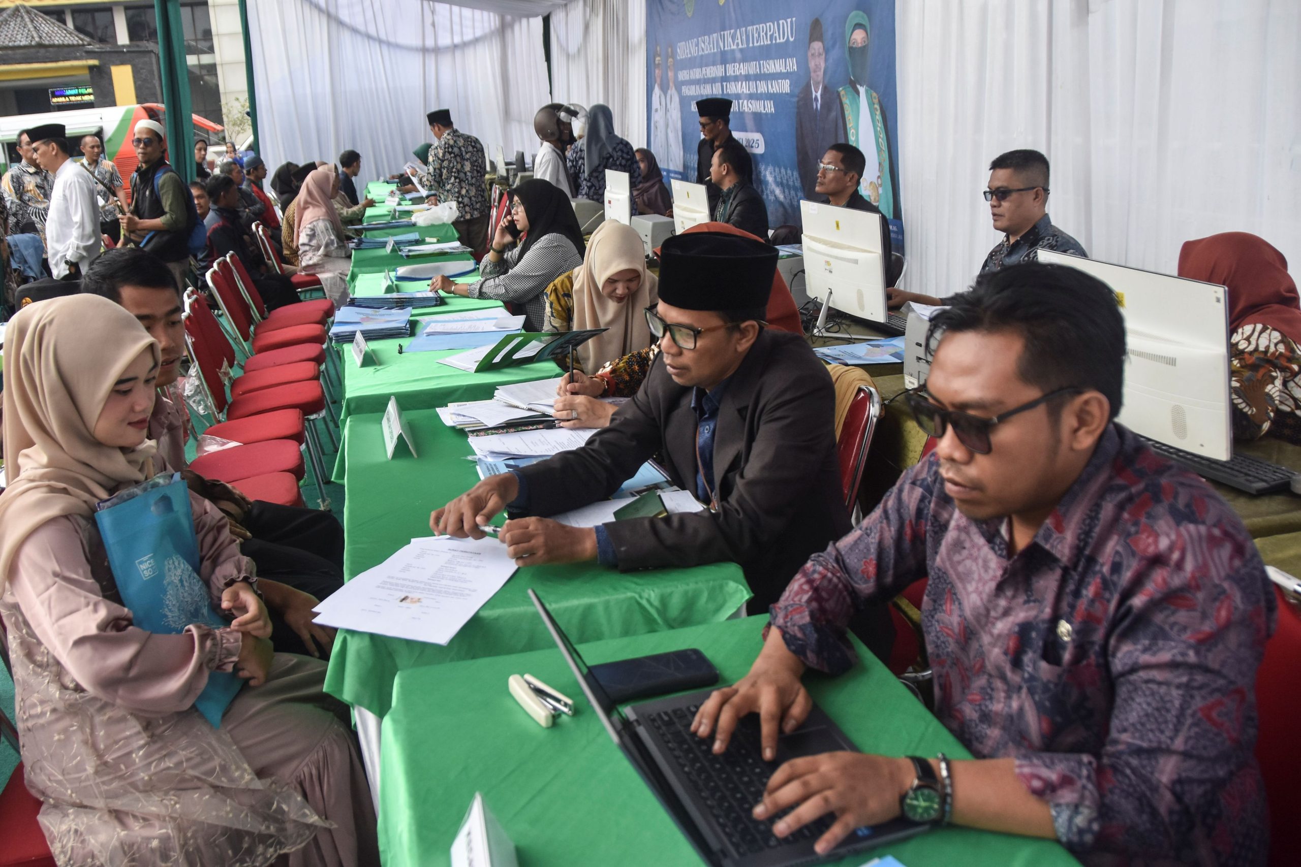 Pegawai Kementerian Agama Kota Tasikmalaya melayani pasangan pengantin saat sidang isbat nikah terpadu di Balai Kota Tasikmalaya, Jawa Barat, Kamis (22/5/2025). Pemkot Tasikmalaya bekerja sama dengan Pengadilan Agama dan Kementerian Agama menggelar sidang isbat nikah terpadu gratis yang diikuti 133 pasangan untuk membantu masyarakat mendapatkan legalitas dan administrasi pernikahan sesuai dengan ketentuan yang berlaku. ANTARA FOTO/Adeng Bustomi/tom. 
